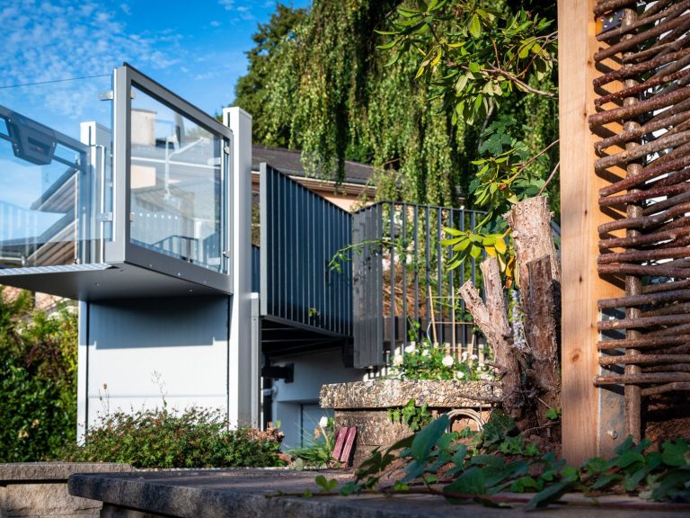 Moderne Architektur mit transparenter Veranda und üppiger Vegetation im Hintergrund.